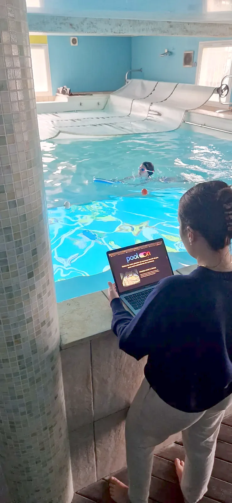A coach runs a projected swim lesson from a tablet at the pool edge