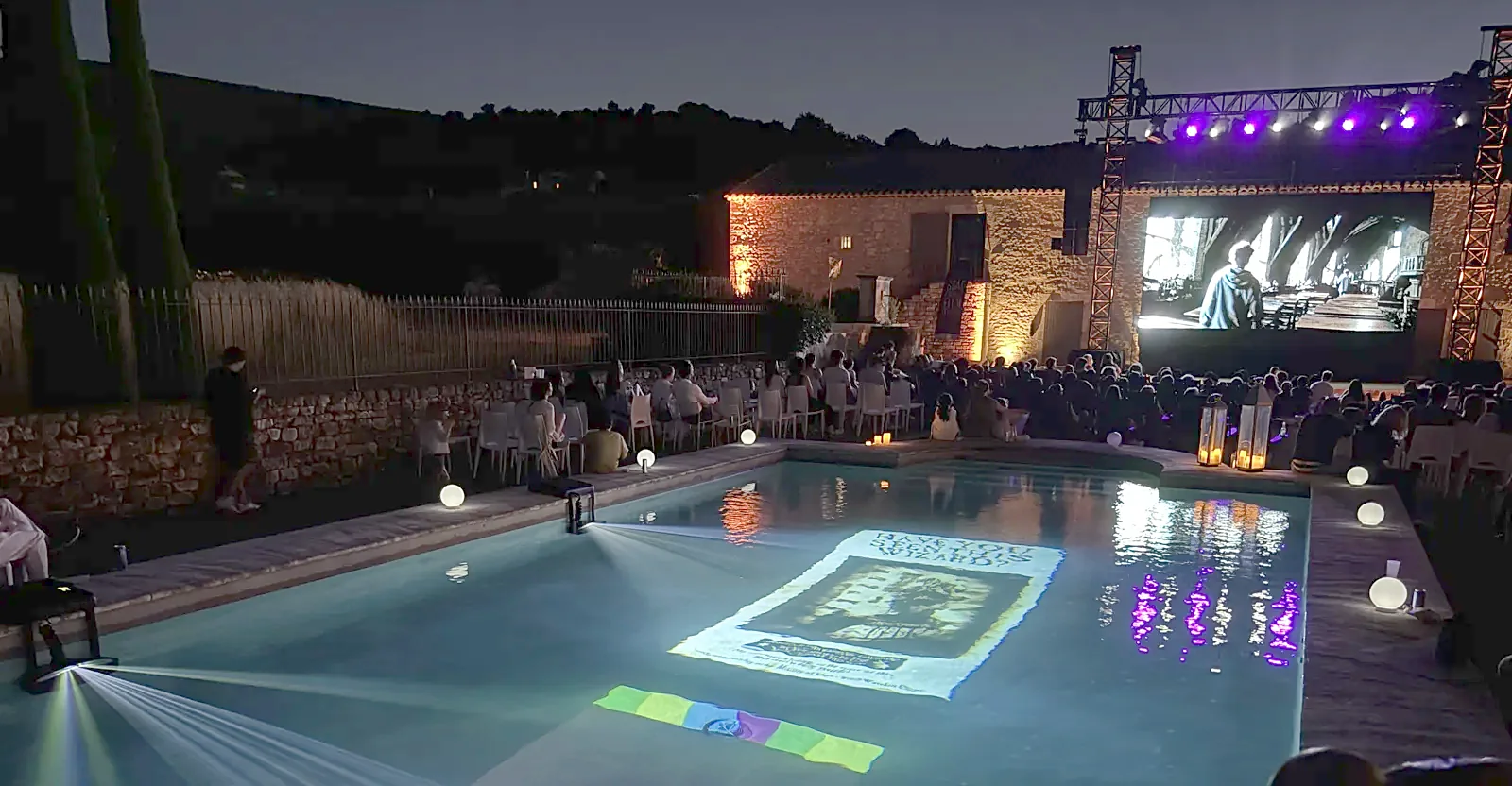 Pool-On projectors projecting festival content into a pool at night, in front of an open-air cinema screen