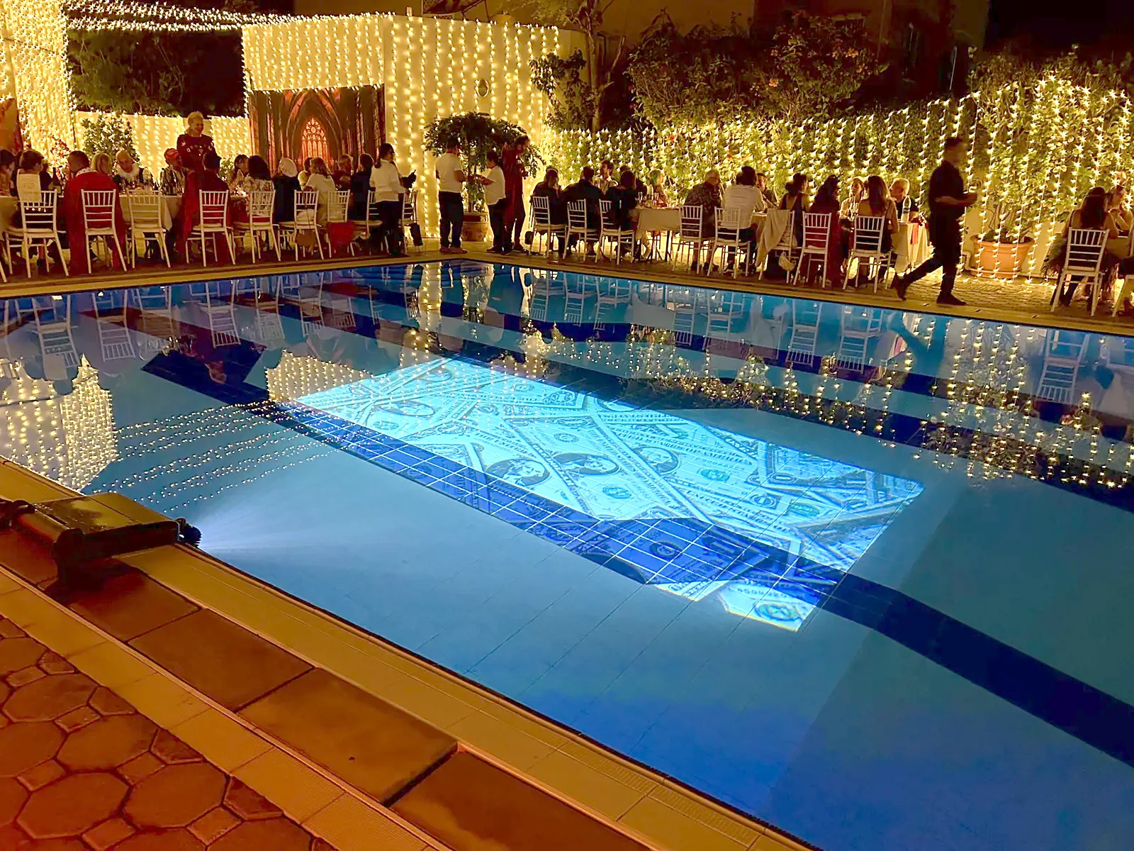 Guests dining around a hotel pool at night while a Pool-On projector projects images under the water